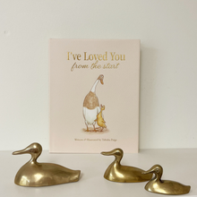 Load image into Gallery viewer, A children's book titled 'I've Loved You from the start' by Tabitha Page stands upright against a plain light wall, with three brass duck figurines arranged in front of it on a white surface.