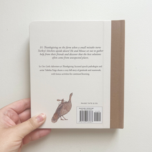 Load image into Gallery viewer, Back cover of a book held in a hand, showing a beige background with printed text, a turkey illustration, and a barcode. The spine is visible on the right and reads PAIGE TATE &amp; CO.