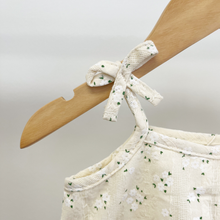 Load image into Gallery viewer, Close-up of a cream-colored floral lace top hanging on a wooden hanger, featuring a delicate decorative bow at the shoulder.