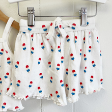 Load image into Gallery viewer, A close up of the shorts of a white pointelle baby top and shorts set with bomb pop popsicle print on hangers against a white background.