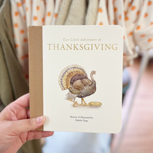 Load image into Gallery viewer, A hand holds a children's board book titled "Our Little Adventure at Thanksgiving" by Talasha Paige. The book has a cream cover with a brown spine, gold lettering, and an illustration of a turkey standing next to a pie.