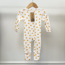 Load image into Gallery viewer, The back of a baby long-sleeve footless one-piece sleeper in white, covered in a small orange pumpkin print, hanging on a wooden hanger against a light gray wall. A Graice Lou, paper brand tag, is attached to the neckline.