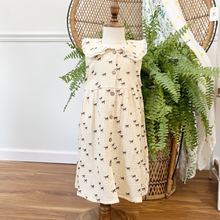 Load image into Gallery viewer, A toddler size muslin dress with a horse print on a cream dress styled on a mannequin in front of a green fern inside a children's boutique, Gracie Lou.