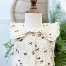 Load image into Gallery viewer, Details of the collar of a toddler size muslin dress with a horse print on a cream dress styled on a mannequin in front of a green fern inside a children's boutique, Gracie Lou.
