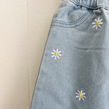 Load image into Gallery viewer, A close up detail of the embroidered daisies on a pair of light wash blue denim baby girl pants.